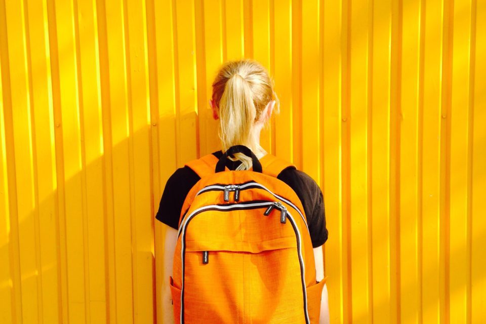 A person with a backpack standing in front of a yellow wall.