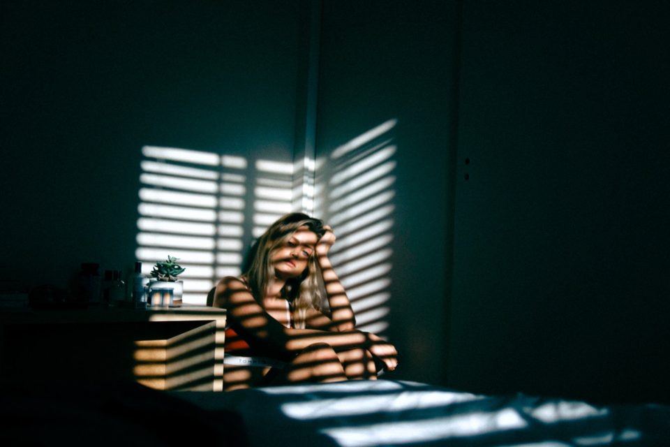 A woman sitting in front of a window with blinds.