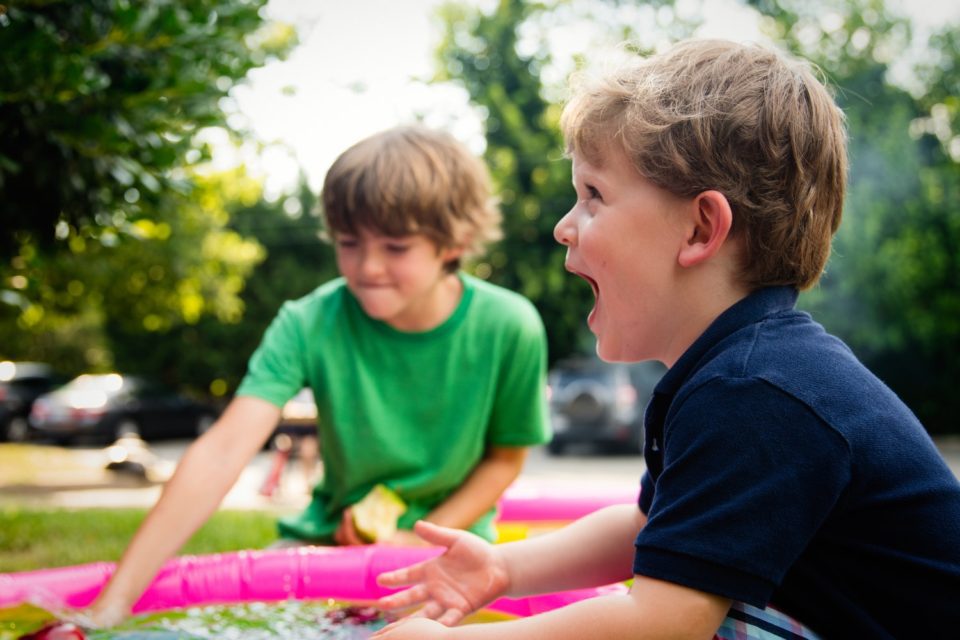 Two young boys playing with a pink water toy.