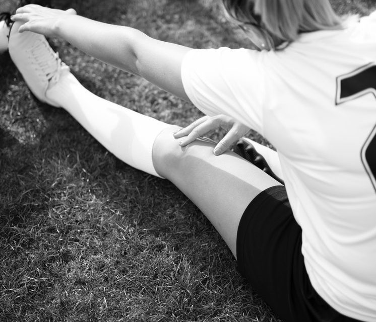 A person stretching on the ground in black and white.