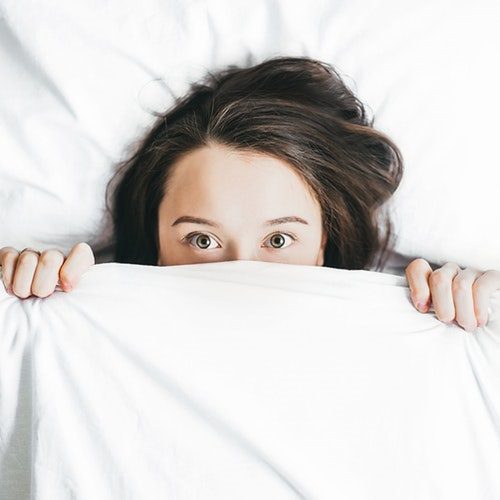 A woman hiding under the covers in bed.