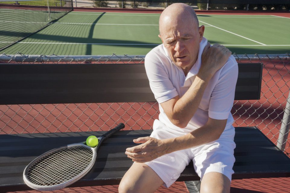 A man sitting on the ground with his tennis racket in hand.
