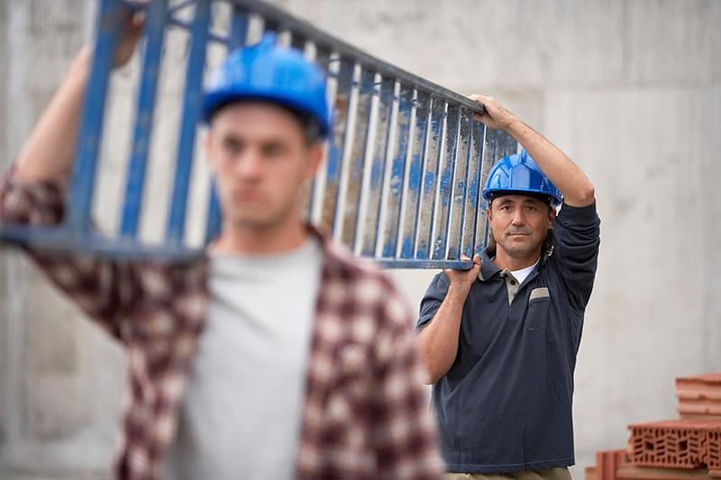 Two men in hard hats and one is holding a ladder.