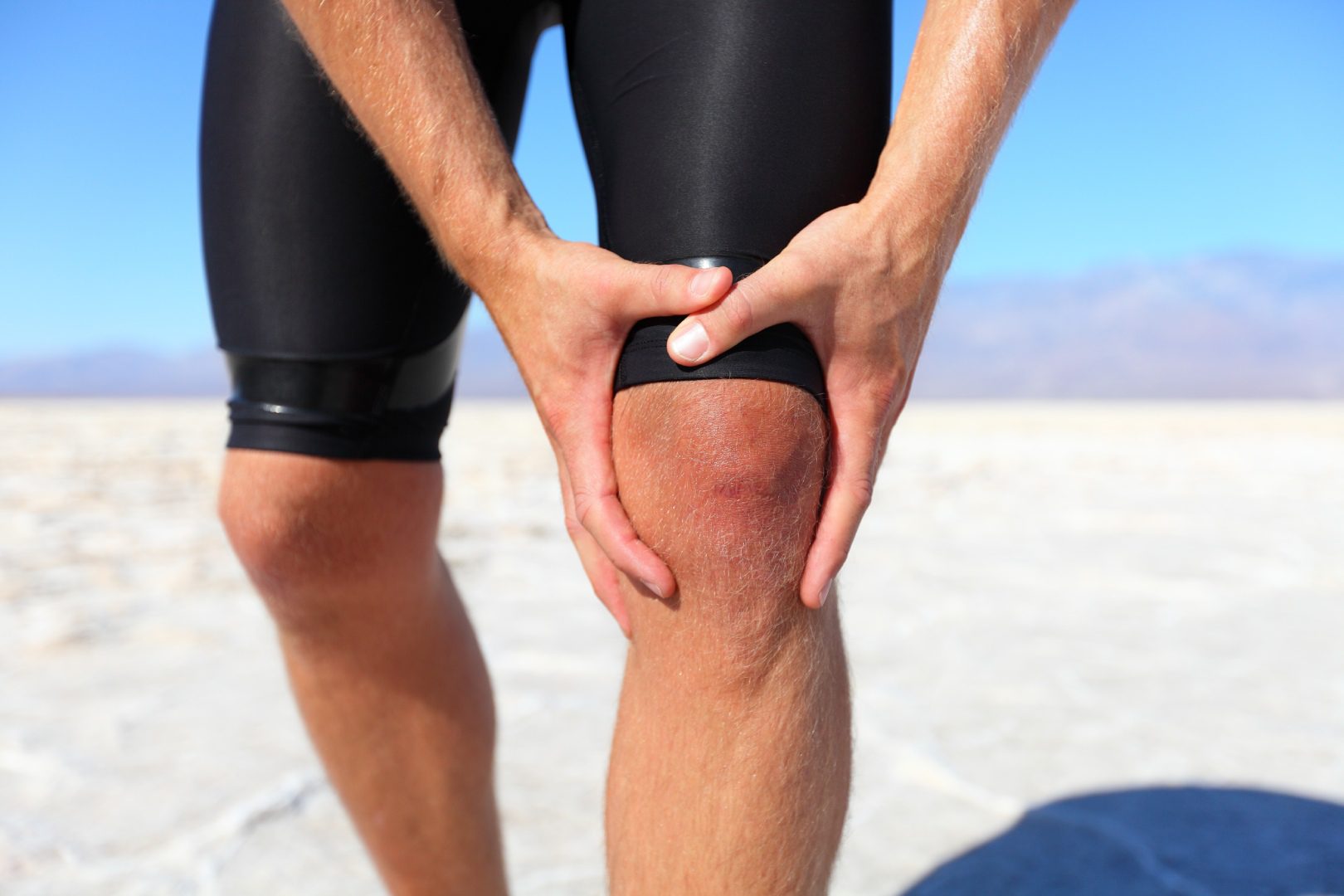 A man holding his knee in the desert.